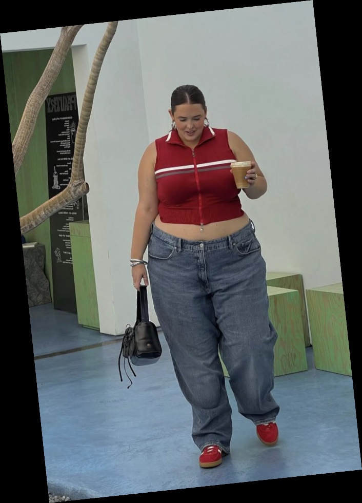 A plus size woman wearing Red sleeveless zip-up knit vest with white and grey horizontal stripes Loose-fit medium wash blue jeans Red sneakers with gum soles Small black leather handbag Silver hoop earrings Silver bangles
