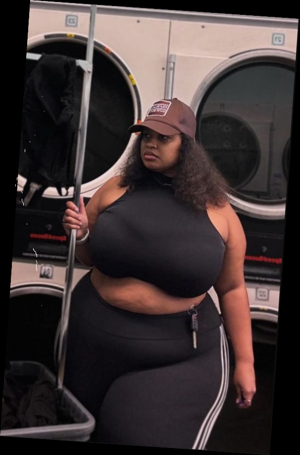 A plus size woman in Brown and beige mesh panel trucker hat Black halter-neck crop top Black leggings with triple side-stripes Brown and beige mesh panel trucker hat Black halter-neck crop top Black leggings with triple side-stripes