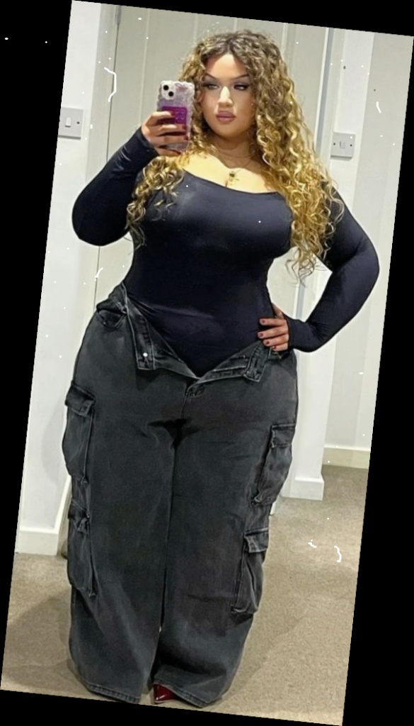 A Plus Size woman in Black long sleeve square neck, bodysuit, Black wide leg, cargo jeans, Red heels, Gold necklace