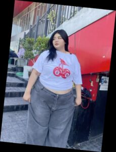 For the baddie girlies, here are some ways to eat up that baddie look 4 A plus size woman in White short sleeve t-shirt with cherry graphic Grey wide leg jeans Gold chain necklace