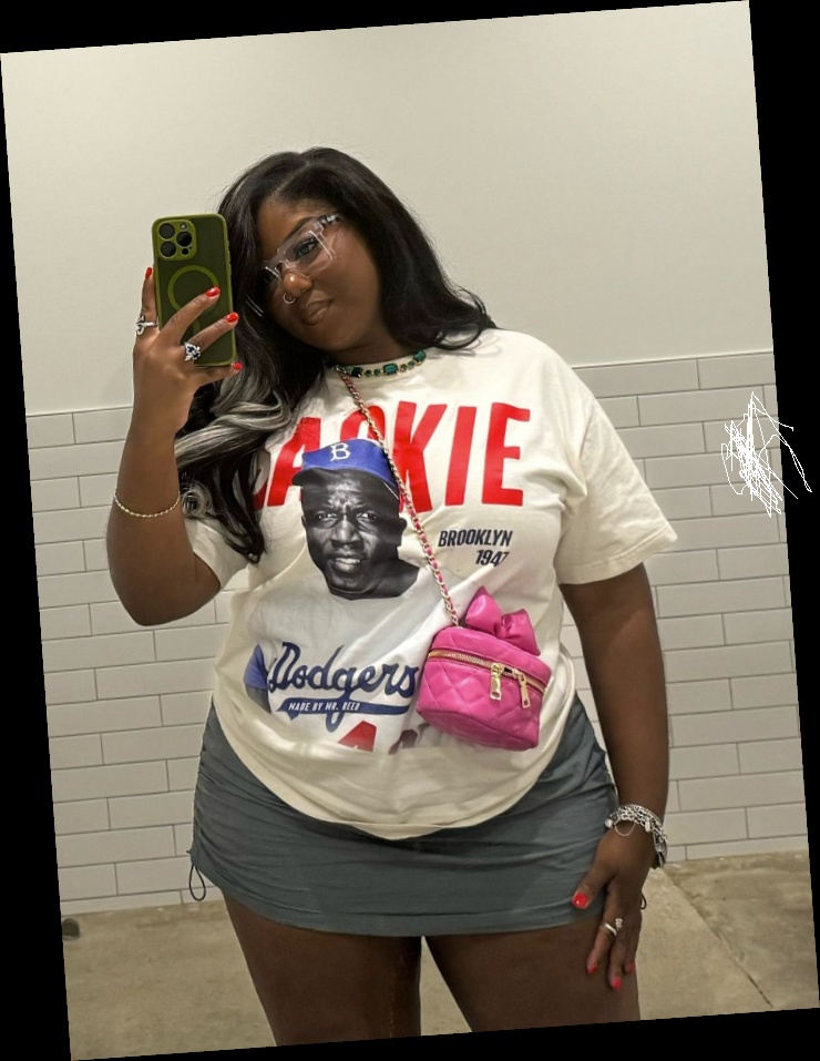 Right here are some pretty much affordable outfits for every plus size queen 7 A plus size woman wearing White "JACKIE" Dodgers graphic t-shirt Grey ruched mini skirt Small pink quilted heart-shaped crossbody bag Clear frame glasses Emerald green bead necklace Silver bracelets