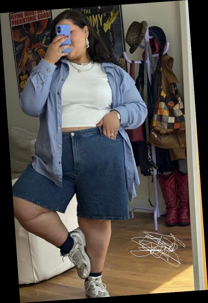 Ideal summer outfit for plus size women 9 A plus size woman wearing Blue and white pinstripe button-down shirt White crewneck crop top Dark wash denim bermuda shorts White New Balance sneakers Navy blue crew socks Silver watch Silver layered necklaces