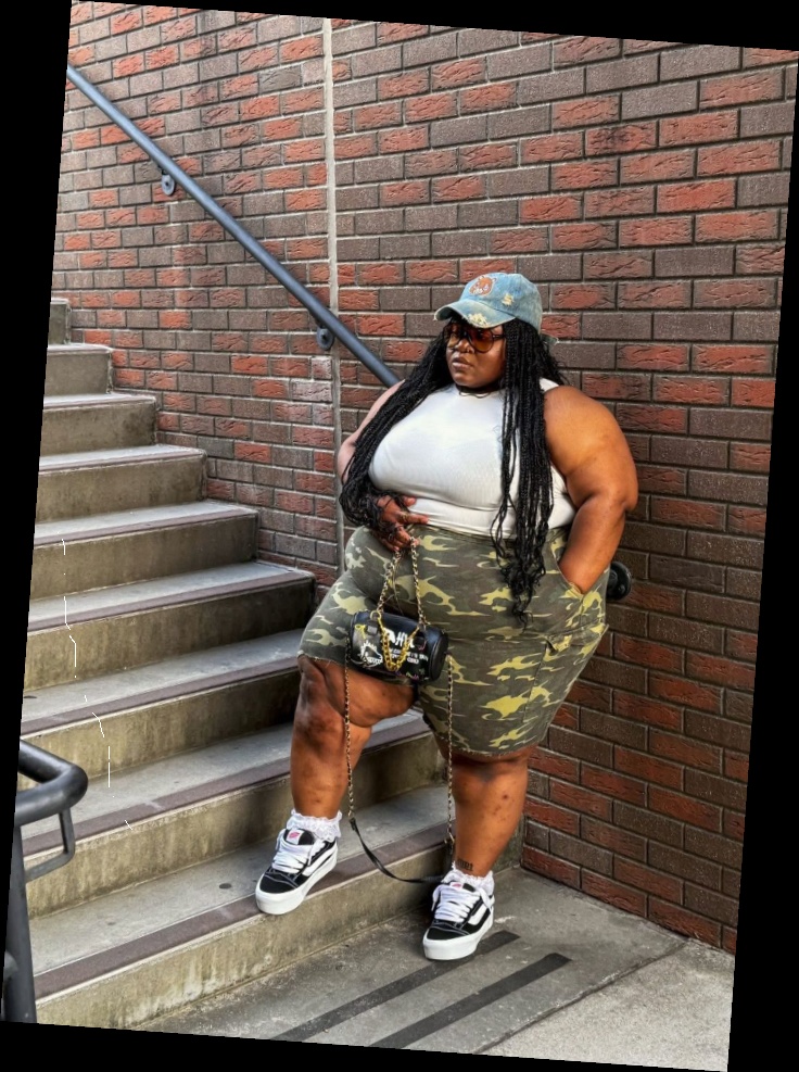A plus size woman wearing Light wash blue denim baseball cap

White ribbed tank top

Camouflage cargo shorts

Black and white platform sneakers (Vans style)

Small black and green graffiti-pattern barrel bag

Gold chain necklace