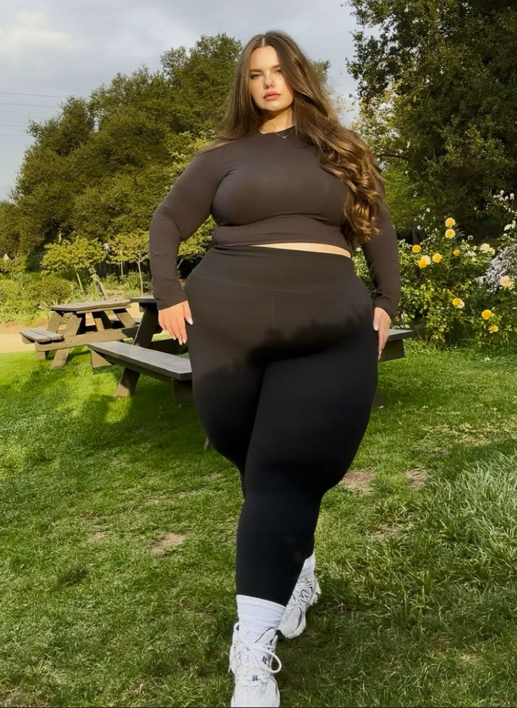 A plus size woman wearing Dark brown crewneck long-sleeve crop top

High-waisted black athletic leggings with a wide waistband

White crew socks

White chunky athletic sneakers

Delicate gold chain necklace