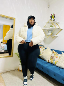 A plus size woman wearing Off-white textured sherpa cropped puffer jacket with a high collar Light blue cropped crewneck sweatshirt High-waisted black cotton-blend leggings Black and white high-top leather sneakers Black unstructured baseball cap