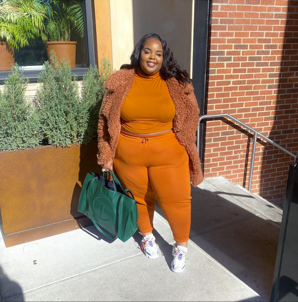 A plus size woman wearing Burnt orange turtleneck crop top
Matching burnt orange slim-fit jogger leggings
Burnt orange textured teddy bear longline coat
Emerald green faux-leather oversized tote bag
White chunky lifestyle sneakers with red and blue accents