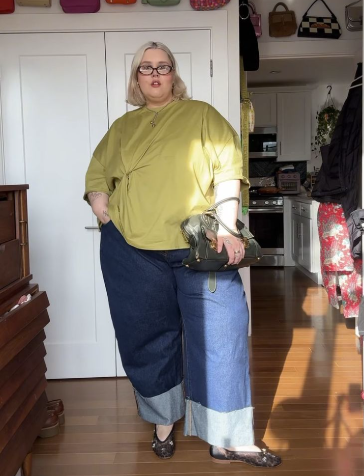 A plus size woman wearing Olive green oversized bomber jacket with drop shoulders

White cropped rib-knit tank top

High-waisted distressed light-wash boyfriend jeans

White chunky platform sneakers

Black leather micro shoulder bag

Gold thick hoop earrings