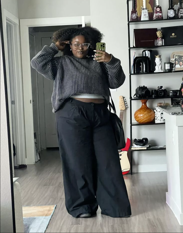 A plus size woman wearing Grey ribbed knit cropped crewneck sweater

White crewneck cropped undershirt

Black ultra-wide leg slouchy trousers

Black leather hobo shoulder bag

Clear frame square eyeglasses

Black casual sneakers