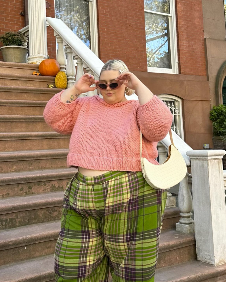A plus size woman wearing Pink chunky knit cropped sweater

Green and purple plaid wide-leg pants

White faux-croc crescent shoulder bag

Pink frame oval sunglasses

White rectangular hair claw clip