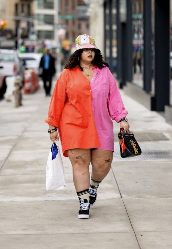 A plus size woman wearing Pink and orange color-block oversized button-down shirt dress

Pastel patchwork pattern bucket hat

Black high-top canvas sneakers

White crew socks with black stripes

Black leather top-handle bag with graphic embroidery