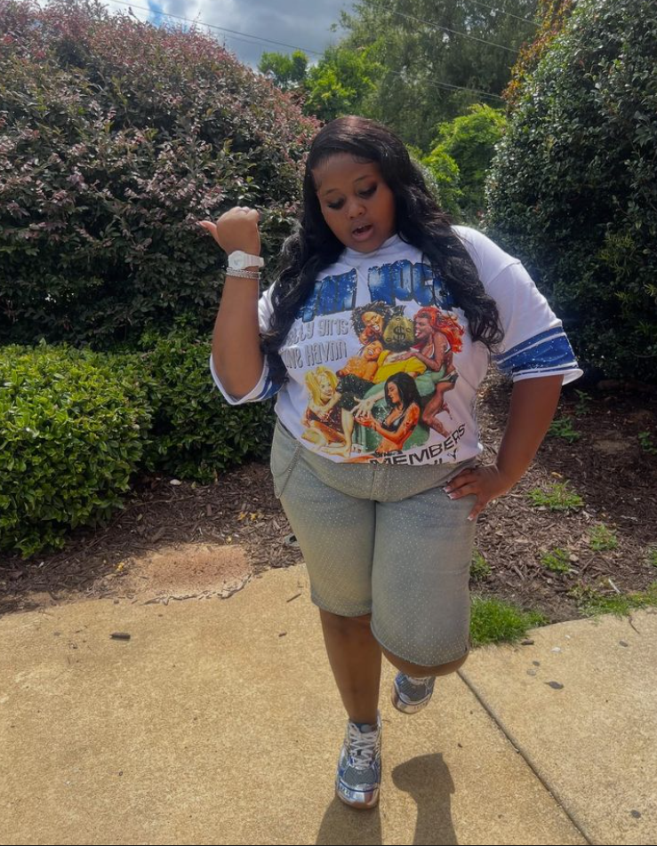 A plus size woman wearing White graphic print oversized T-shirt with blue sleeve stripes
Light grey rhinestone embellished denim long shorts
Metallic silver running sneakers
White chunky sports watch
Silver tennis bracelet