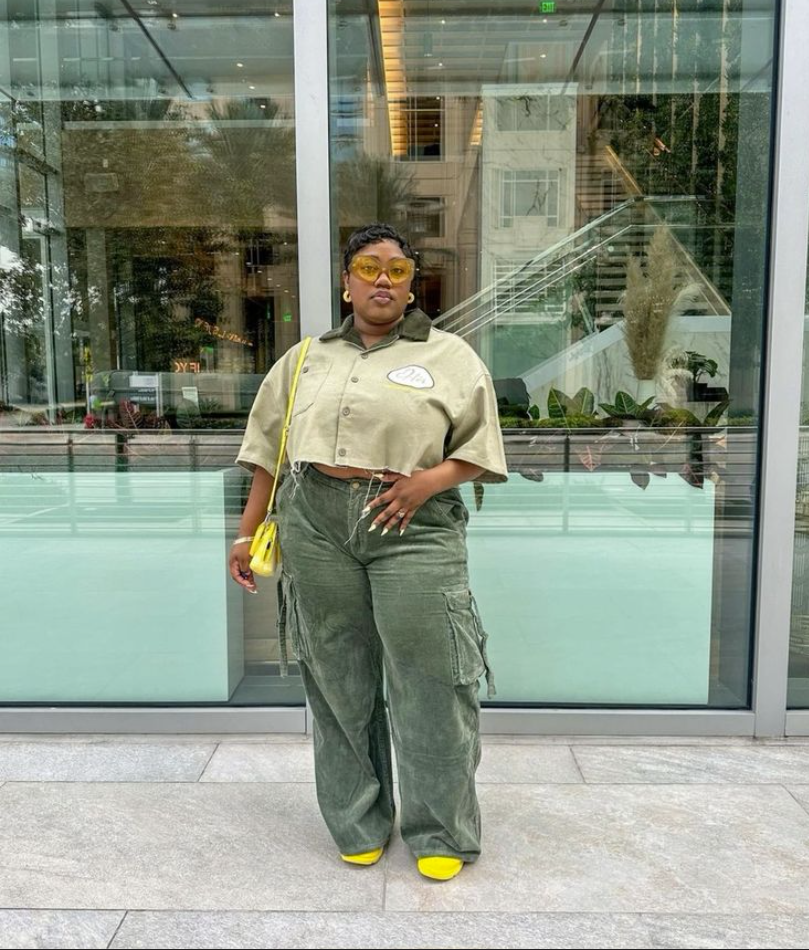 A plus size woman wearing Olive green cropped short-sleeve button-up shirt with dark collar

Sage green corduroy wide-leg cargo pants

Bright yellow mini crossbody bag

Yellow transparent frame sunglasses

Bright yellow sneakers

Gold hoop earrings