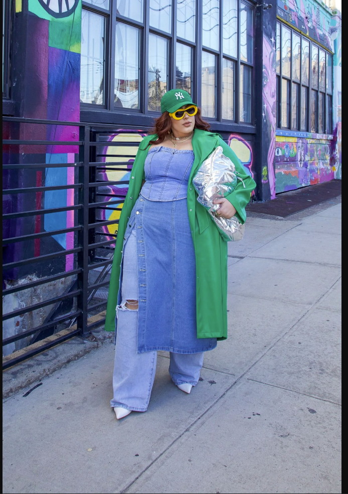 A plus size woman wearing Bright green trench coat

Strapless denim corset top

Front-button denim maxi skirt with slit

Wide-leg light wash distressed jeans

White pointed-toe heeled mules

Green NY baseball cap

Chunky yellow rectangle sunglasses

Silver metallic puffy cloud bag