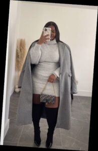 A plus size woman in Light grey turtleneck sweater mini dress Longline heather grey wool overcoat Black over-the-knee boots Designer monogram flap handbag with gold chain strap Gold rings