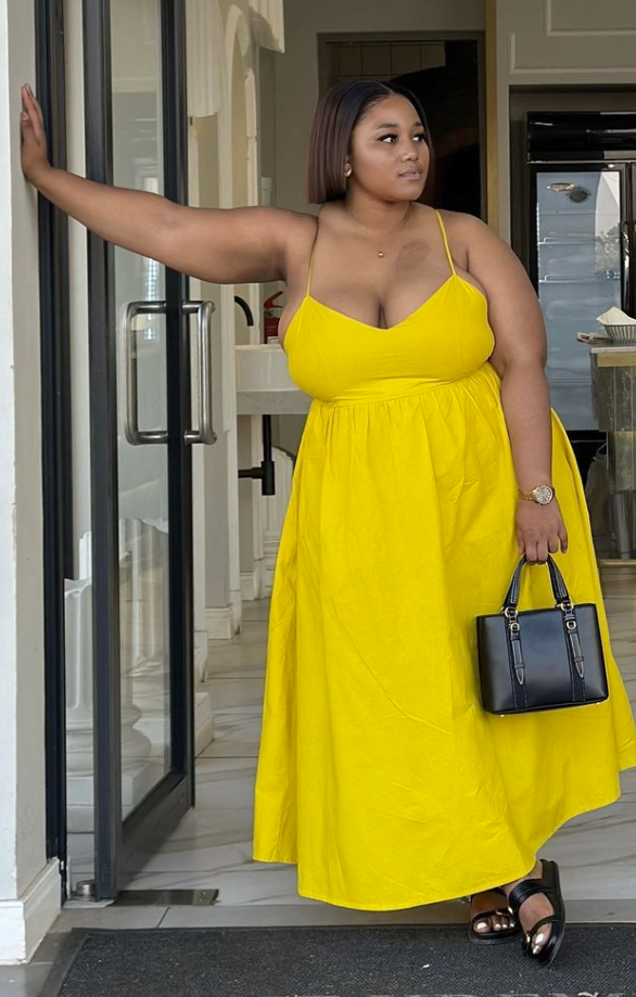Sun-Ready Summer Vacation Outfits for Plus Size Women 2 A plus size woman wearing Bright yellow cami maxi dress with spaghetti straps and empire waist Black leather top-handle mini tote bag Black leather slide sandals with thick straps Gold watch with a link bracelet Delicate gold pendant necklace Gold stud earrings