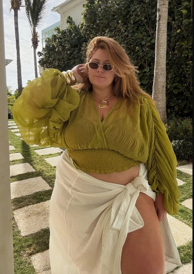 Sun-Ready Summer Vacation Outfits for Plus Size Women 7 A plus size woman wearing Olive green sheer crinkled cropped blouse with oversized bell sleeves White linen wrap sarong maxi skirt with a side tie Black mesh bikini top / bralette (visible underneath) Oversized black rectangular sunglasses Chunky gold statement collar necklace Thick stacked gold bangle bracelets