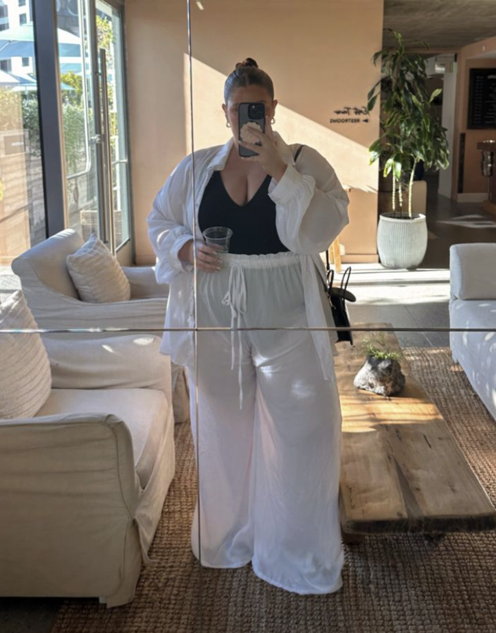 Sun-Ready Summer Vacation Outfits for Plus Size Women 8 A plus size woman wearing White oversized linen button-up shirt White sheer wide-leg palazzo pants with a drawstring waist Black low-cut tank top / one-piece swimsuit Black leather shoulder bag Gold hoop earrings