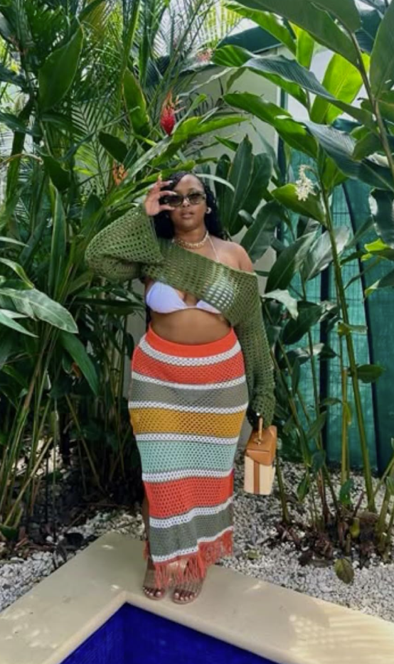 Sun-Ready Summer Vacation Outfits for Plus Size Women 10 A plus size woman wearing Olive green open-knit crochet cropped shrug sweater with long flare sleeves Multi-colored striped crochet knit maxi skirt with fringe hem (orange, yellow, mint, white, olive) White triangle bikini top Two-tone leather and straw structured top-handle box bag Oversized black sunglasses Gold chain choker necklace Beige slide sandals