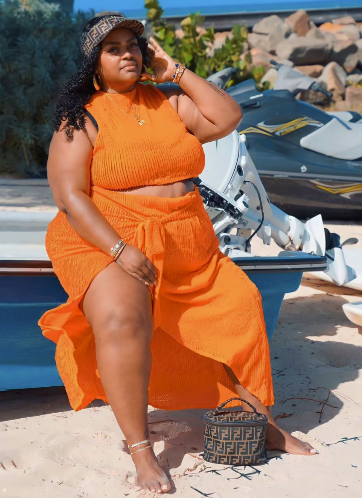 Sun-Ready Summer Vacation Outfits for Plus Size Women 11 A plus size woman wearing Bright orange sleeveless ribbed knit cropped tank top Bright orange matching textured maxi wrap skirt with a high slit and front tie Brown and black luxury monogram print visor hat Brown and black luxury monogram print cylindrical bucket bag Gold delicate chain necklaces Gold and beaded stack bracelets Gold metallic ankle bracelet / anklet