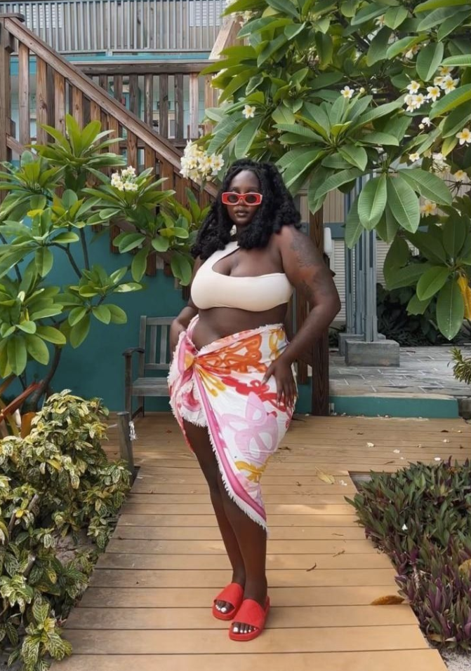 Beach Queen Energy: Stylish Outfits for Plus Size Women by the Sea 3 A plus size woman wearing Cream off-the-shoulder one-strap bikini top
Vibrant pink, orange, and yellow abstract floral print sarong wrap skirt with frayed edges
Bright red thick-frame rectangular sunglasses
Red flat slide sandals