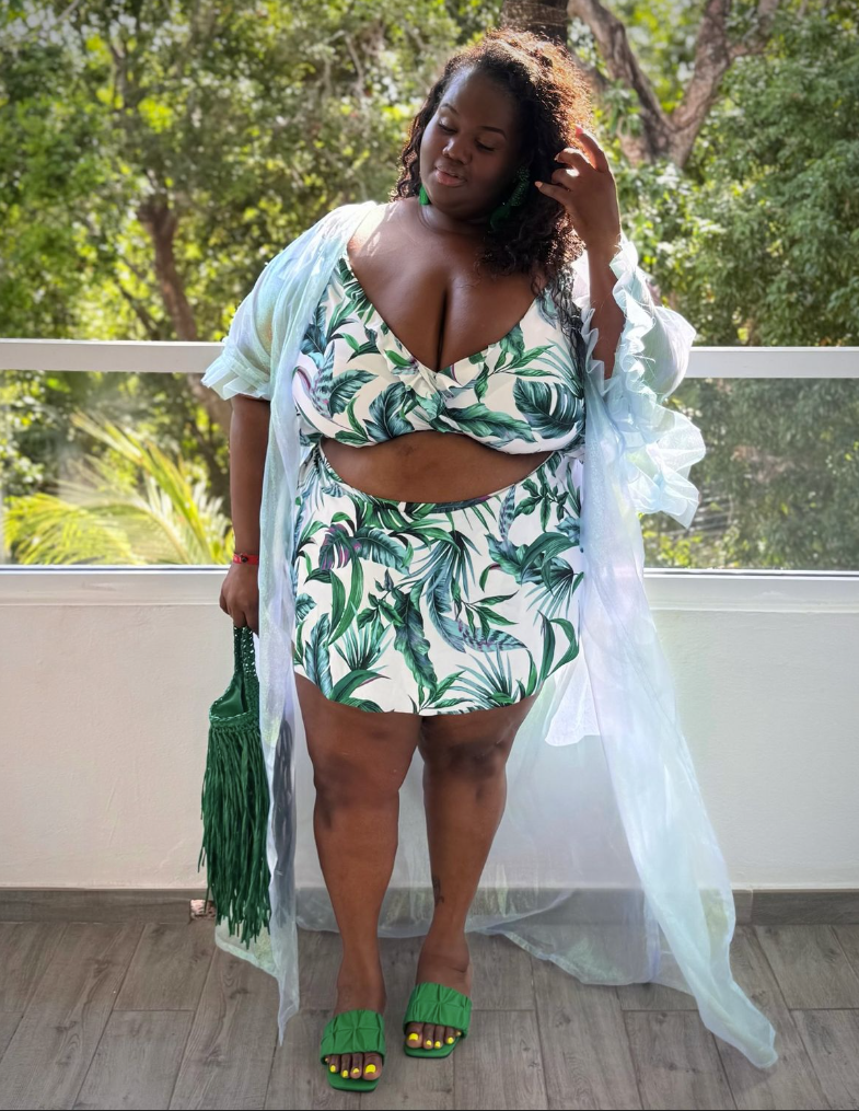 Beach Queen Energy: Stylish Outfits for Plus Size Women by the Sea 4 A plus size woman wearing Green and white tropical palm leaf print bikini top with front knot detail
Matching green and white palm leaf print high-waisted mini skirt cover-up
Sheer light mint green maxi duster cardigan with ruffled trim
Emerald green woven macrame fringe tote bag
Green textured slide sandals
Deep green statement earrings