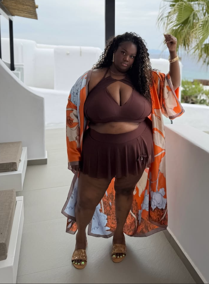 Beach Queen Energy: Stylish Outfits for Plus Size Women by the Sea 11 A plus size woman wearing Chocolate brown halter neck wrap bikini top with a keyhole front cutout
Matching chocolate brown pleated high-waisted swim skirt
Long orange, cream, and light blue floral print satin kimono duster robe
Metallic gold textured flat slide sandals
Thick gold bangle bracelet
Delicate gold chain necklace