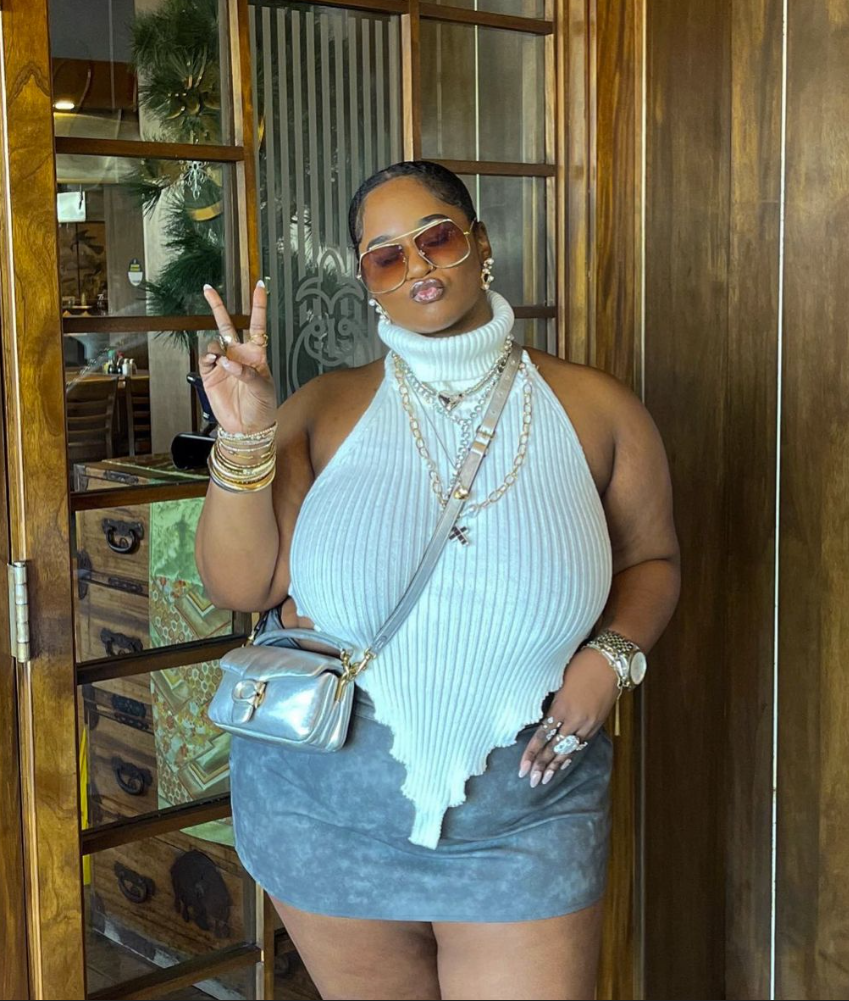 After Dark Glow: Baddie Night Out Outfits for Plus Size Women 9 A plus size woman wearing White ribbed knit turtleneck halter top with an asymmetrical pointed hem
Gray suede mini skirt
Metallic silver quilted crossbody bag with a chain strap
Oversized gold-frame aviator sunglasses
Layered gold chain necklaces with a cross pendant
Stacked gold bangle bracelets
Large silver statement ring
Two-tone luxury watch