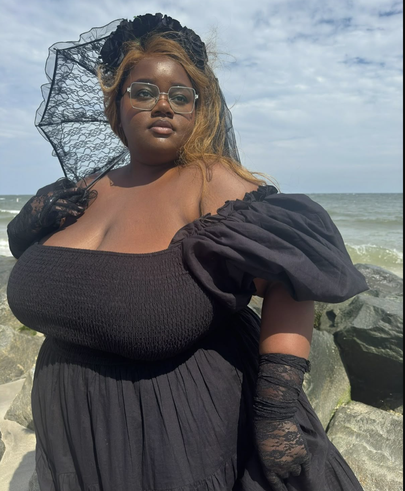 A plus size woman wearing Black off-the-shoulder smocked midi dress with puff sleeves
Black lace wrist-length gloves
Black lace parasol umbrella
Black ruffle floral headband veil
Clear frame square eyeglasses