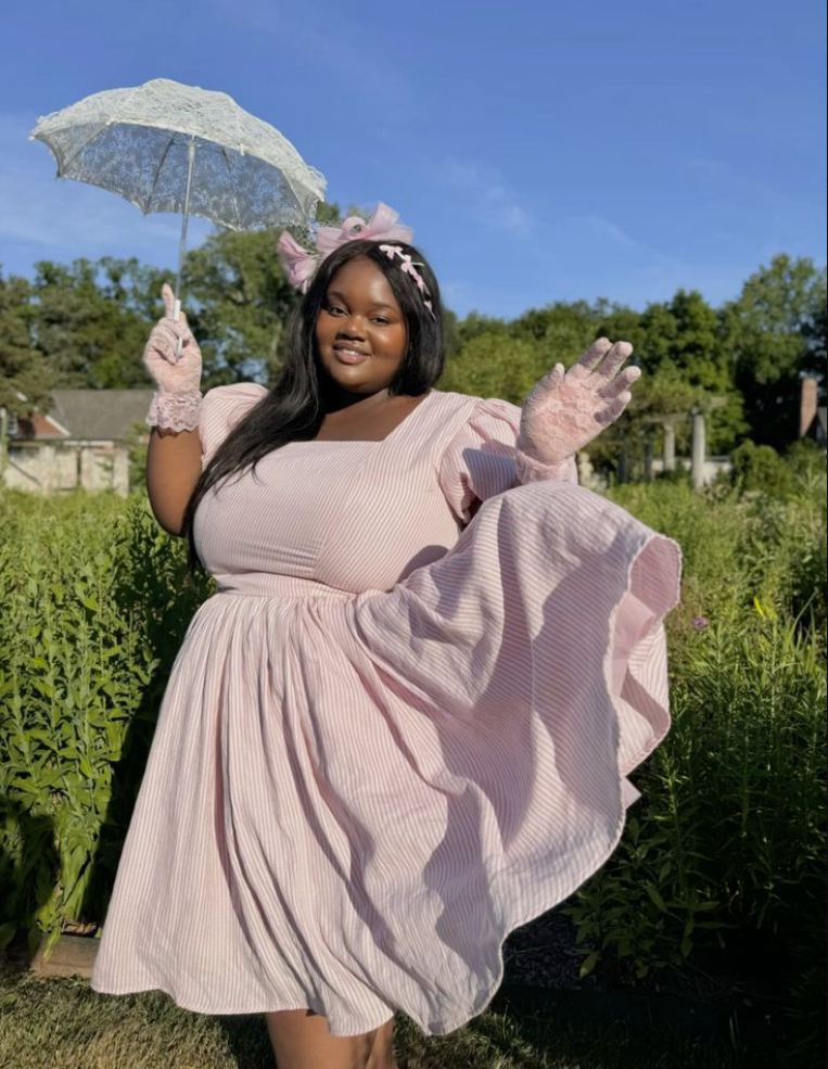 A plus size woman wearing Pink and white striped square neck puff sleeve dress
Pink lace wrist gloves
Pink tulle hair bow fascinator
Pink and white ribbon hairband
White lace parasol umbrella