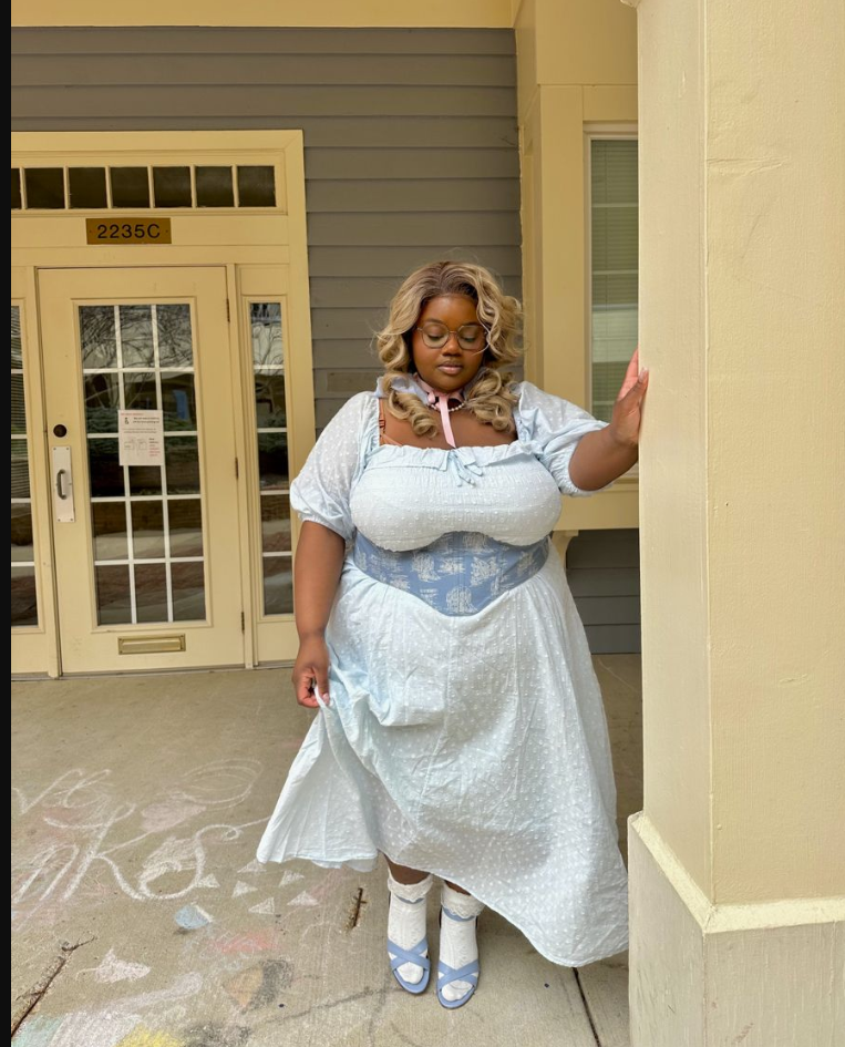 A plus size woman wearing Light blue cotton off-the-shoulder midi dress
Blue and white toile de Jouy corset belt
White lace ruffle ankle socks
Light blue strappy low-heel sandals
Pink ribbon choker necklace
Clear round eyeglasses