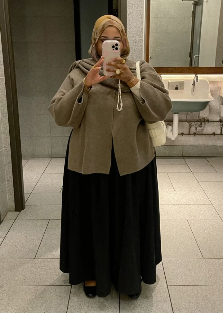 A plus size woman wearing Beige wool-blend coat Black maxi skirt Yellow/gold hijab White top White handbag Gold jewelry