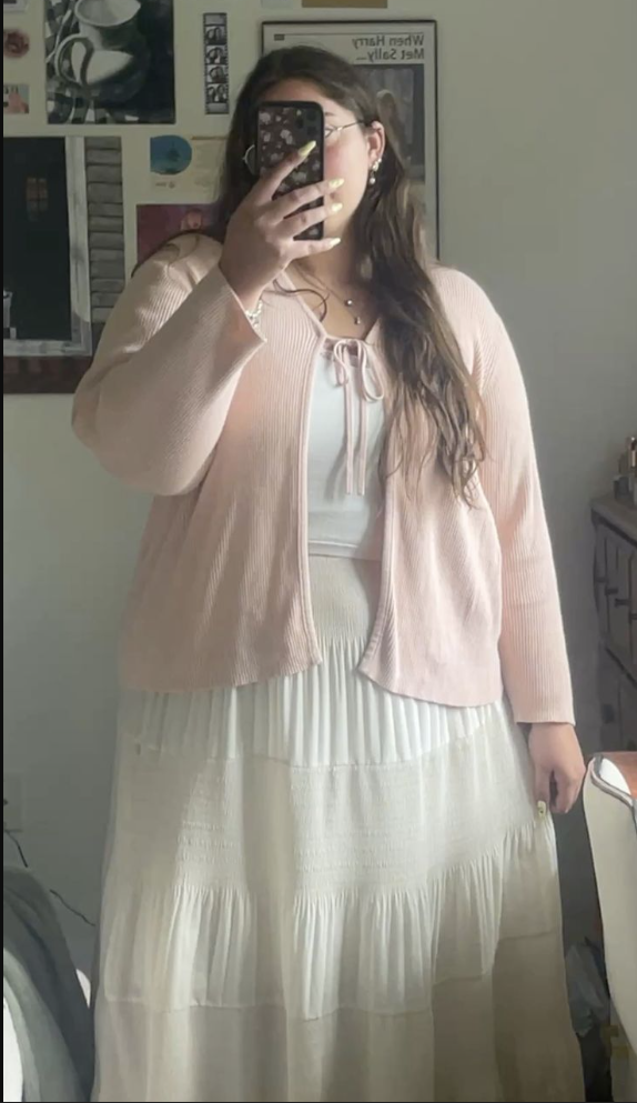 A plus size woman wearing Light pink ribbed cardigan White tie-front camisole White tiered maxi skirt Glasses Pearl earrings and layered necklaces