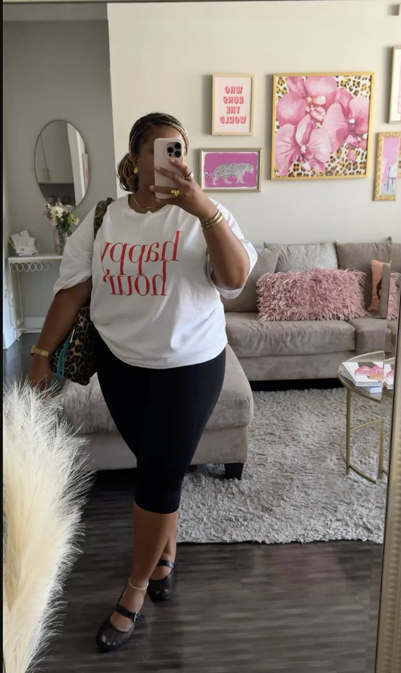 Daytime Charm: Cute & Comfortable Lunch Outfits for Plus Size Women 5 A plus size woman wearing White oversized “happy hour” graphic t-shirt Black high-waisted body fit skirt Black Mary Jane flats Leopard-print crossbody bag Gold hoop earrings Gold bracelets and rings