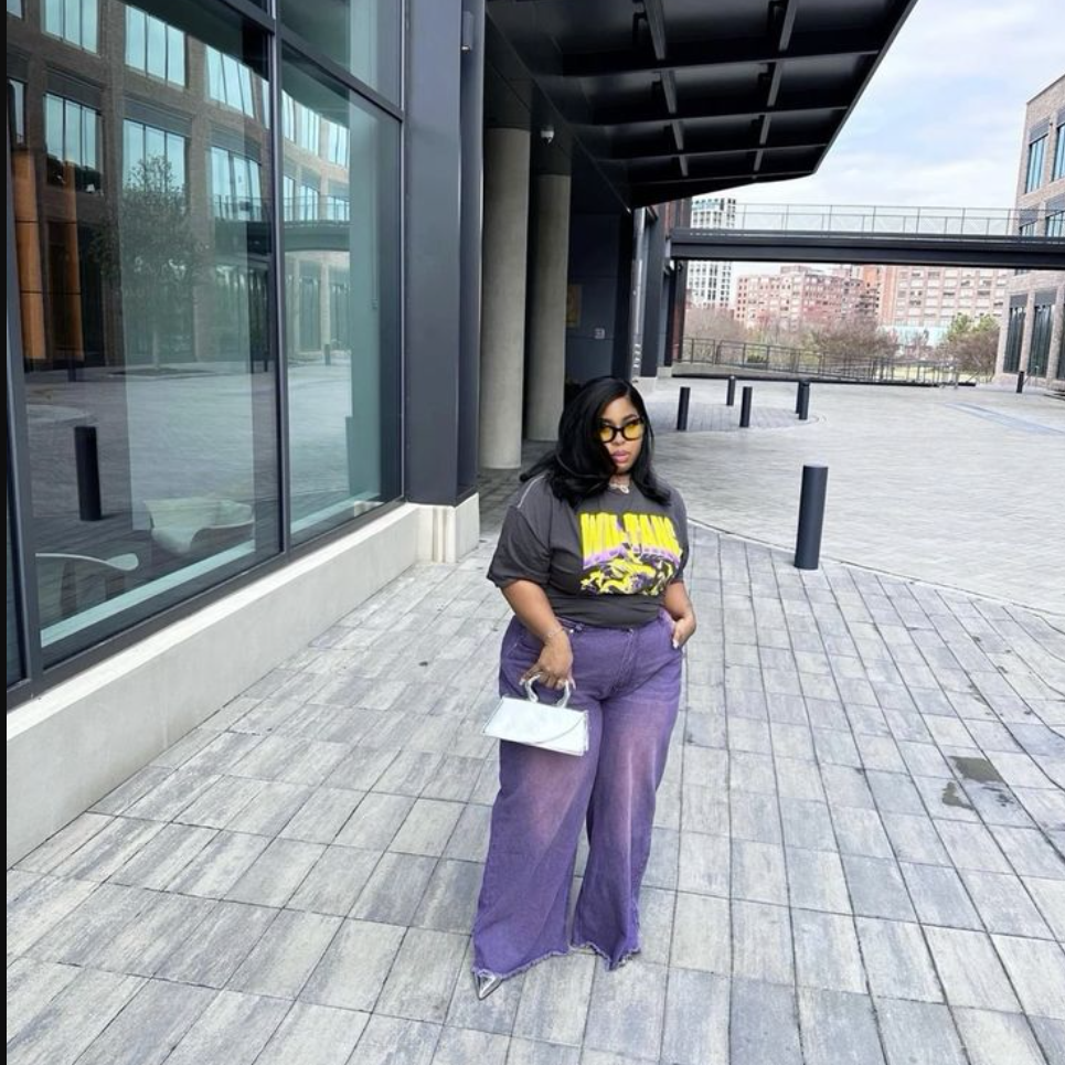 Daytime Charm: Cute & Comfortable Lunch Outfits for Plus Size Women 6 A plus size woman wearing Black oversized graphic t-shirt Purple wide-leg cargo-style pants Yellow-tinted sunglasses White mini handbag Silver jewelry