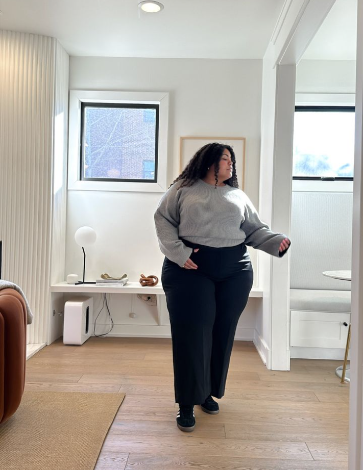 A plus size woman wearing Grey oversized knit sweater
Black high-waisted wide-leg trousers
Black sneakers
Gold hoop earrings