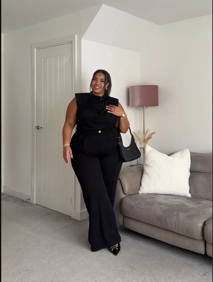 A plus size woman wearing Black sleeveless cowl-neck top
Black high-waisted wide-leg trousers
Black pointed-toe heels with gold detail
Black shoulder bag
Gold jewelry
