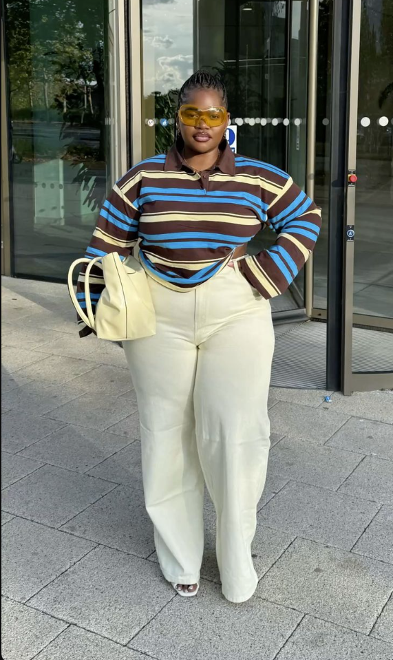 A plus size woman wearing Multi-stripe (brown/blue/yellow) polo shirt
Off-white wide-leg trousers
Yellow-tinted sunglasses
Cream handbag