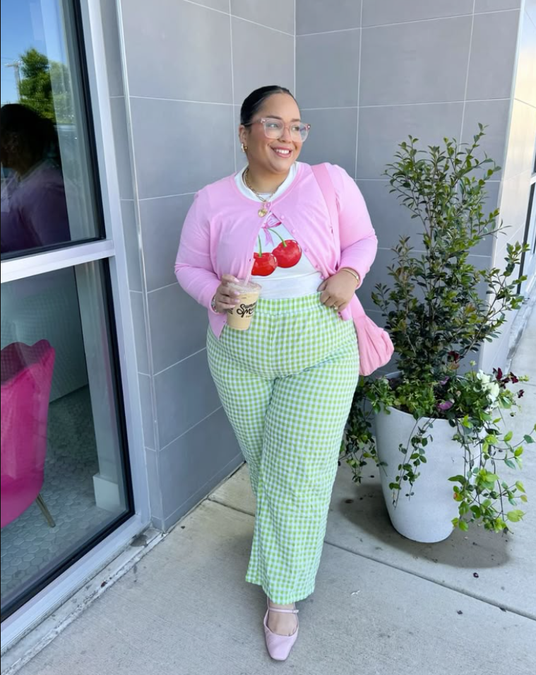 A plus size woman wearing Pink button-up cardigan
White cherry-print t-shirt
Green and white gingham wide-leg pants
Pink pointed-toe flats
Pink shoulder bag
Clear glasses