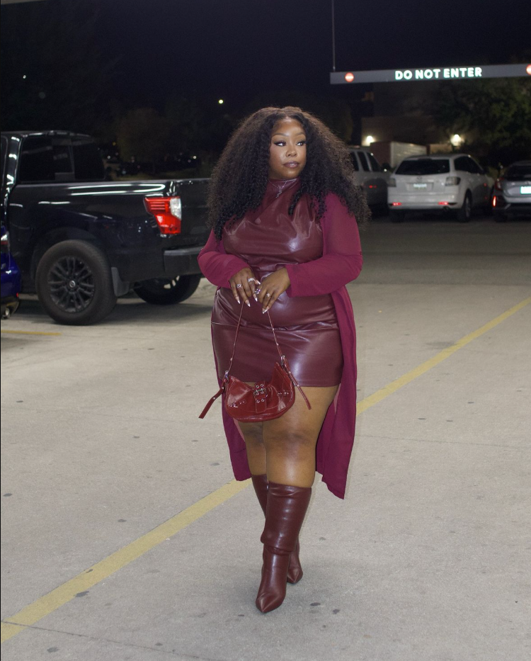 A plus size woman wearing Maroon faux leather high-neck mini dress
Matching maroon long cardigan/duster
Maroon knee-high pointed boots
Maroon mini saddle bag
Long manicured nails