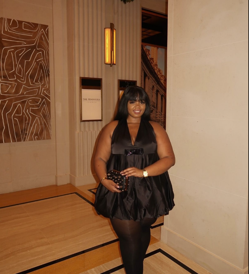 A plus size woman wearing Black satin halter babydoll top with sequin bow
Black sheer tights
Black studded clutch
Gold watch
Gold bracelet