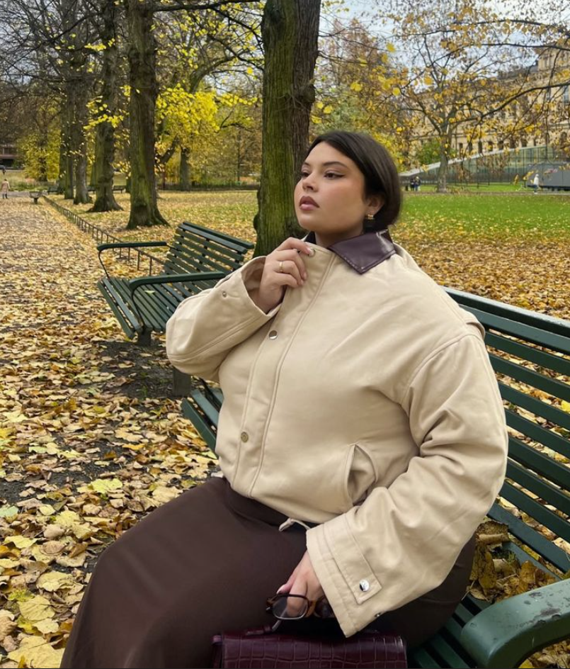 A plus size woman wearing Beige utility jacket with leather collar Brown midi skirt Burgundy crocodile-embossed handbag