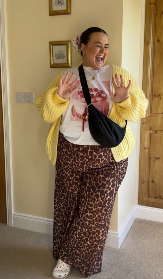 A plus size woman wearing Yellow chunky knit cardigan
Cherry graphic t-shirt
Leopard print wide leg pants
Black crossbody bag
White Crocs