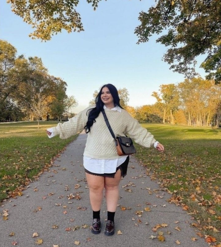 A plus size woman wearing Cream chunky knit sweater
White collared button-up shirt
Black mini skirt with lace trim
Black ankle socks
Dark chunky loafers
Brown crossbody bag
