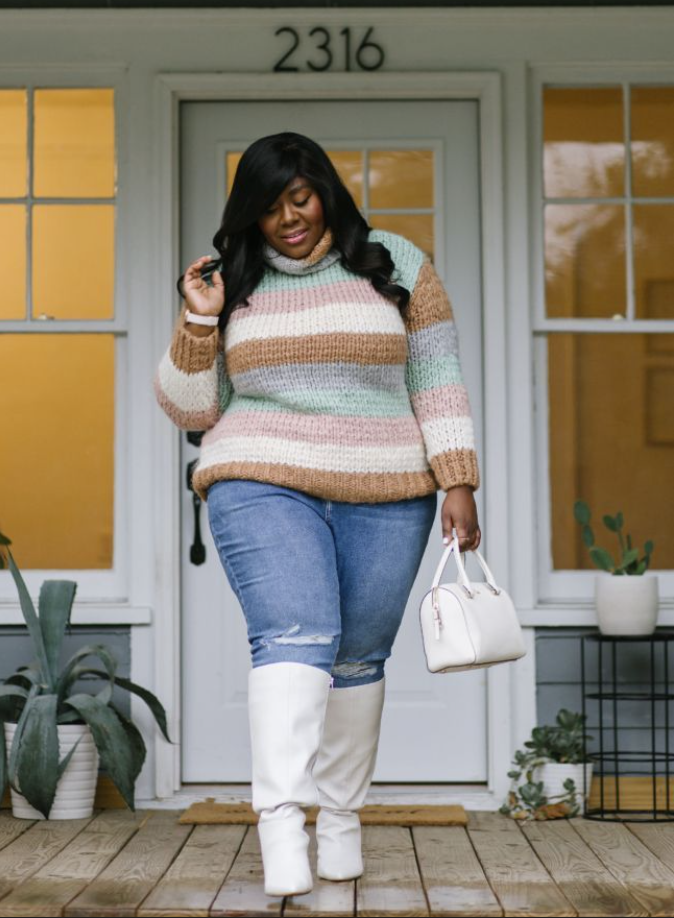A plus size woman wearing Multi-colored striped chunky turtleneck sweater
Light-wash ripped jeans
White knee-high boots
White structured handbag