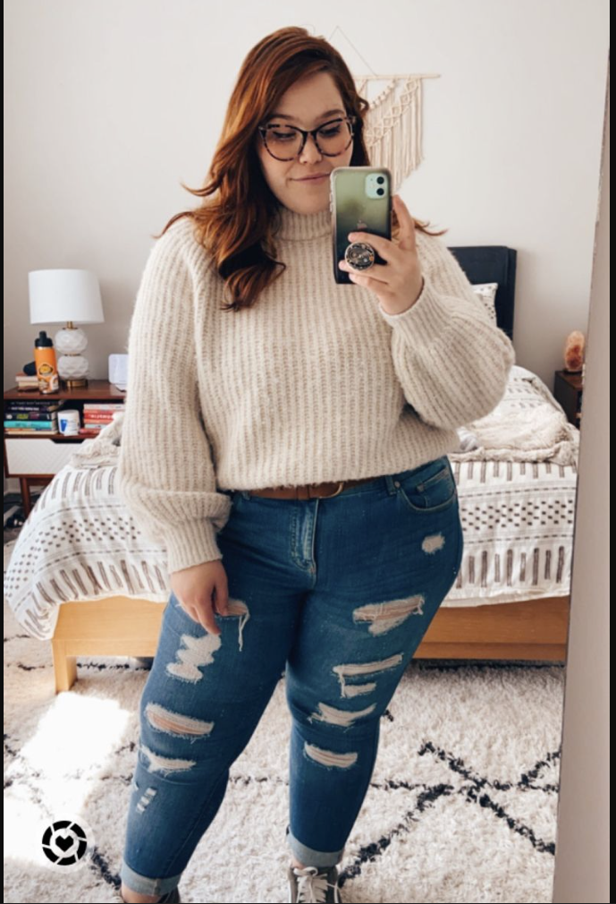 A plus size woman wearing Cream chunky knit turtleneck sweater
Blue ripped jeans
Brown leather belt
Sneakers