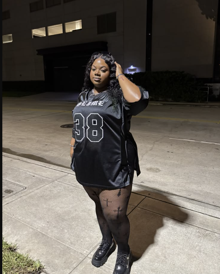 A plus size woman wearing Black oversized football jersey
Black fishnet tights with cross pattern
Black platform chunky boots
Silver chain necklace
Silver bracelets