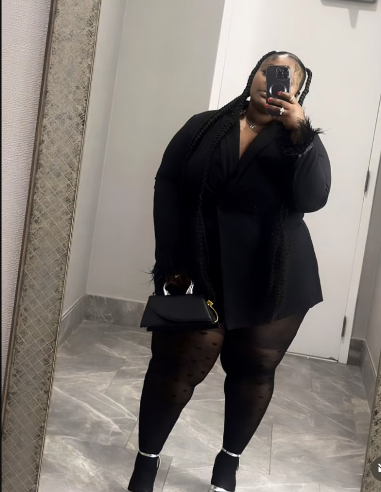 A plus size woman wearing Black wrap blazer mini dress
Black dotted sheer tights
Black ankle boots with silver detail
Black handbag with gold hardware
Silver jewelry
