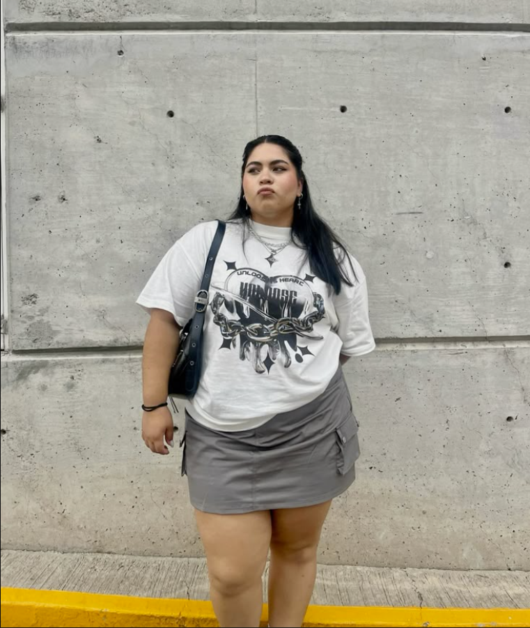 A plus size woman wearing White graphic oversized t-shirt Gray cargo mini skirt Black shoulder bag Silver layered necklaces Silver hoop earrings Black bracelet