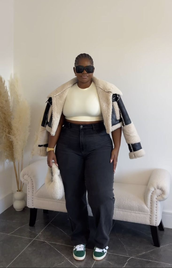 A plus size woman wearing Cream ribbed crop top
Cream and black shearling aviator jacket
Black straight-leg jeans
Green and white sneakers
Black sunglasses
White fluffy handbag