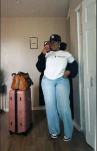 A plus size woman wearing White graphic t-shirt Black long cardigan Light blue wide-leg jeans Black baseball cap with NY logo Clear glasses Black and white sneakers